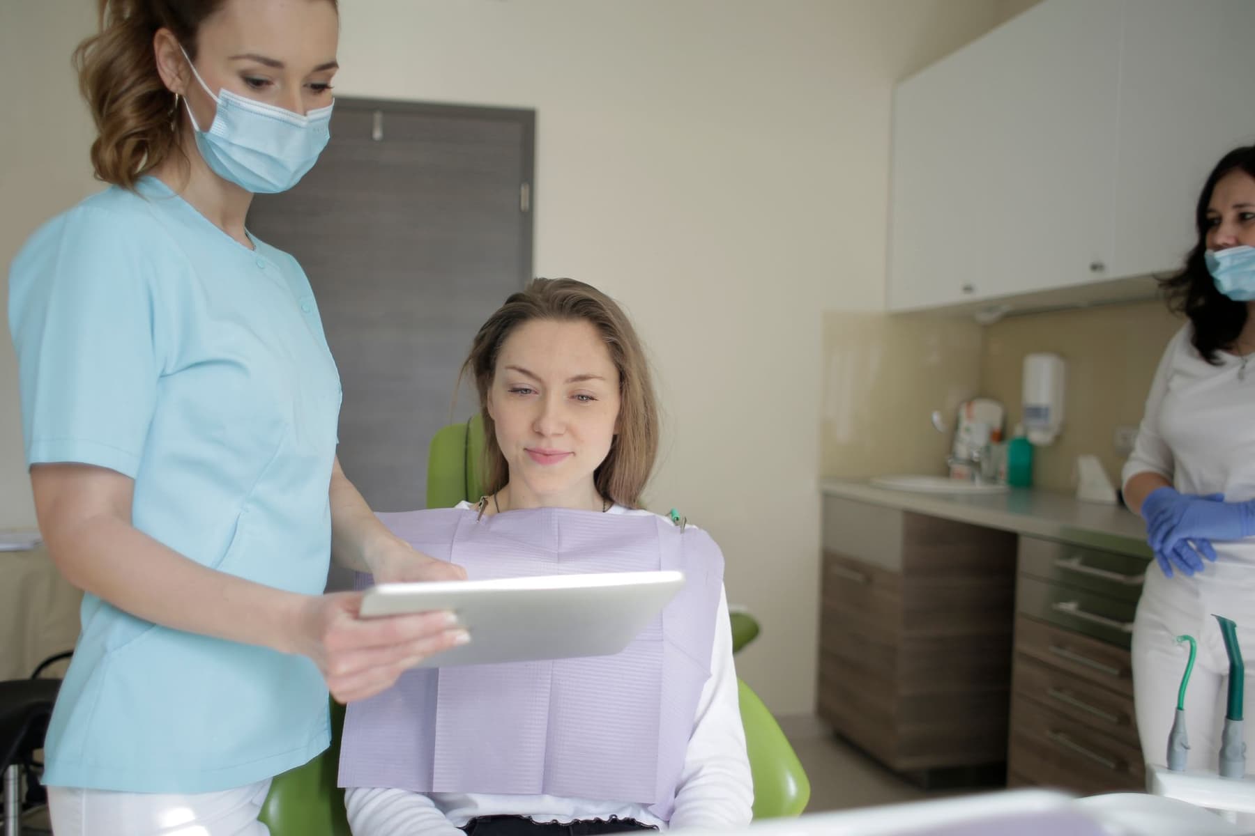 Dentista mostrando a tela do tablet para a paciente na cadeira